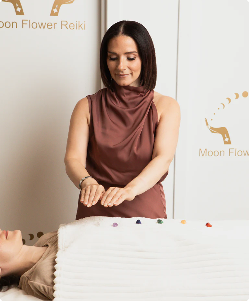 Woman performing Reiki on a client with 'Moon Flower Reiki' branding in the background.